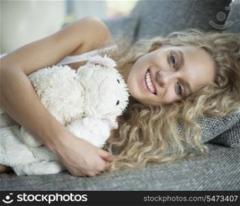 Portrait of young woman with teddy bear lying on sofa