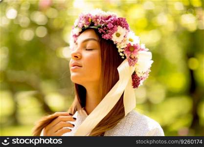 Portrait of young woman with wreath of fresh flowers on head in the park