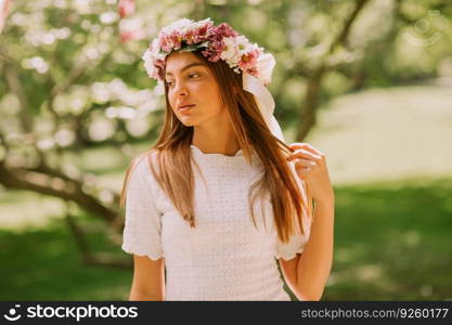 Portrait of young woman with wreath of fresh flowers on head in the park