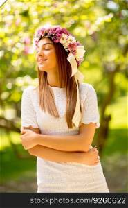 Portrait of young woman with wreath of fresh flowers on head in the park