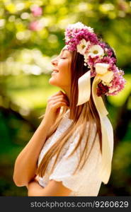 Portrait of young woman with wreath of fresh flowers on head in the park