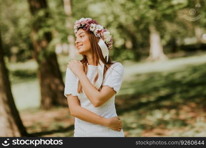 Portrait of young woman with wreath of fresh flowers on head in the park