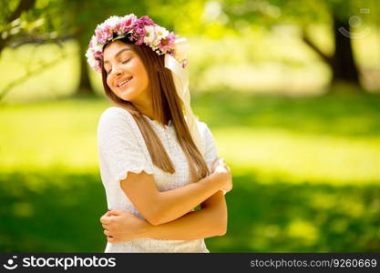 Portrait of young woman with wreath of fresh flowers on head in the park