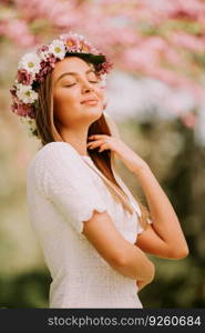 Portrait of young woman with wreath of fresh flowers on head in the park