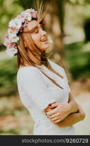 Portrait of young woman with wreath of fresh flowers on head in the park