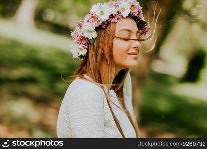 Portrait of young woman with wreath of fresh flowers on head in the park