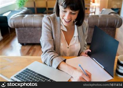 Portrait of young woman working from home with laptop and files. Home office concept. New normal lifestyle.