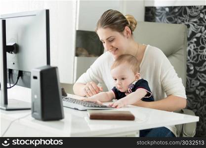 Portrait of young woman working on computer at home office and looking after her baby son. Portrait of woman working on computer at home office and looking after her baby son