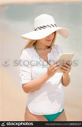 Portrait of young woman working on digital tablet at beach at windy day