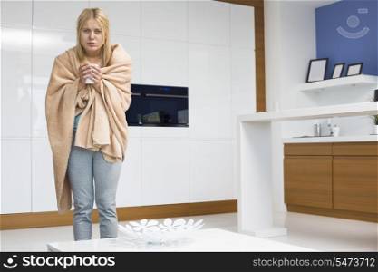 Portrait of young woman wrapped in blanket holding coffee mug in house