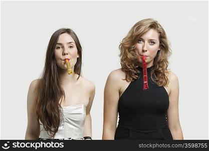 Portrait of young women blowing party puffers against gray background