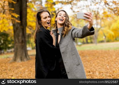 Portrait of young women taking selfie with mobile phone in the autumn park