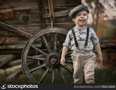 Portrait og a little, cute gentleman posing over a wooden carriage