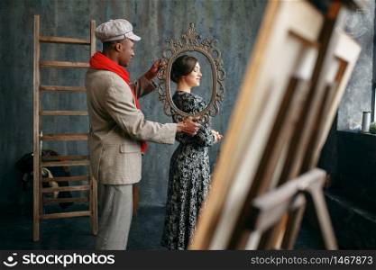 Portrait painter holds frame, female model in art studio. Male artist standing at his workplace, creative master in workshop. Portrait painter holds frame, female model