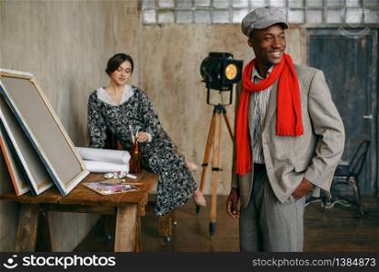 Portrait painter in a red scarf and female model in art studio. Male artist standing at his workplace, creative master in workshop. Portrait painter and female model in art studio