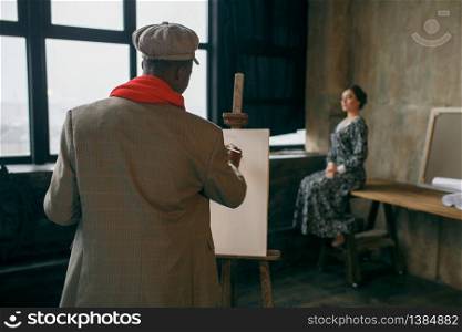 Portrait painter with brush draws female model. Male artist standing at his workplace, creative master at the easel in workshop. Portrait painter with brush draws female model