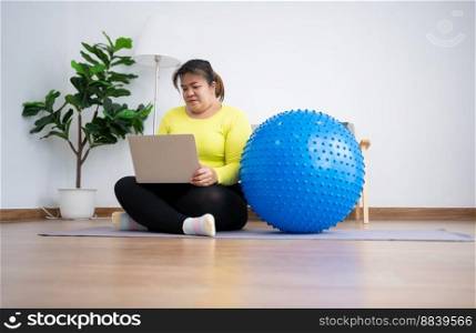 Portrait plus size woman user computer laptop for join fitness class for exercise with fitness ball in home gym. Technology and communication, Healthcare and weight loss concept.