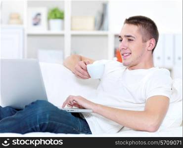 portrait profile of smiling young man with cup of coffee using laptop at home