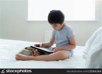 Portrait School kid sitting in bed reading the story on tablet, Young boy having fun playing game on digital pad,Happy child relaxing in bedroom in the morning,Home schooling or Online Education concept
