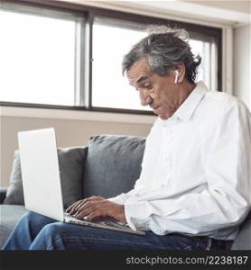 portrait senior man sitting sofa wearing bluetooth earphone using laptop
