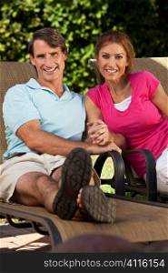 Portrait shot of an attractive, successful and happy middle aged man and woman couple in their thirties, sitting togther holding hands and smiling.