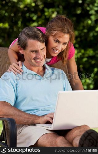 Portrait shot of an attractive, successful and happy middle aged man and woman couple in their thirties, sitting togther outside using a laptop computer.