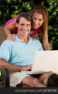 Portrait shot of an attractive, successful and happy middle aged man and woman couple in their thirties, sitting togther outside using a laptop computer.