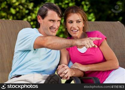 Portrait shot of an attractive, successful and happy middle aged man and woman couple in their thirties, sitting togther holding hands and smiling while the man is pointing off camera.