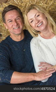 Portrait shot of an attractive, successful and happy middle aged man and woman couple sitting laughing together on hay or straw bales