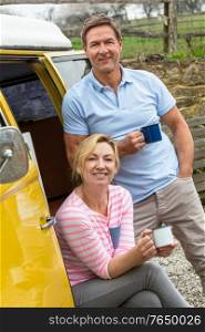 Portrait shot of an attractive, successful and happy middle aged man and woman couple together drinking tea or coffee standing by a camper van bus