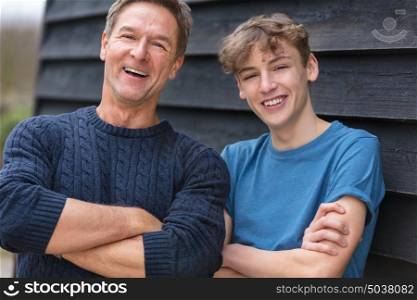 Portrait shot of an attractive, successful and happy middle aged man father male arms folded with his teenage boy son outside laughing teen, wearing a blue sweater and t-shirt