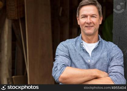 Portrait shot of an attractive, successful and happy middle aged man male arms folded outside wearing a blue shirt outside his garage or shed