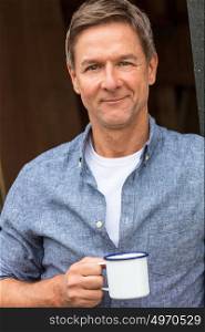Portrait shot of an attractive, successful and happy middle aged man male wearing a blue shirt drinking tea or coffee from a tin cup