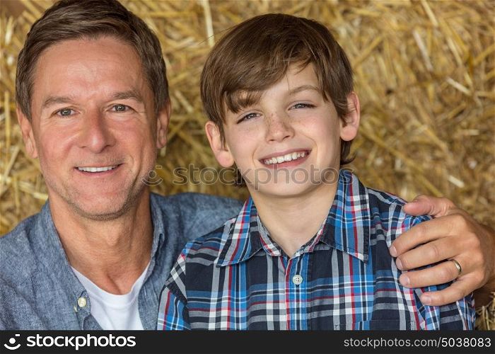 Portrait shot of an attractive, successful and happy middle aged man male sitting on hay bales with his male child boy son in a barn or stables