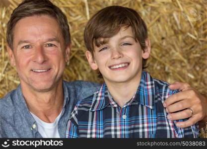 Portrait shot of an attractive, successful and happy middle aged man male sitting on hay bales with his male child boy son in a barn or stables