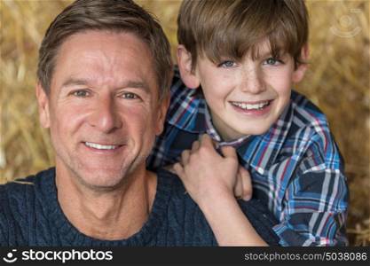 Portrait shot of an attractive, successful and happy middle aged man male wearing a blue sweater sitting on hay bales with his male child boy son in a barn or stables