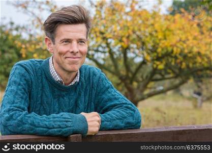 Portrait shot of an attractive, successful and happy middle aged man male arms folded outside leaning on a fence or gate in the country
