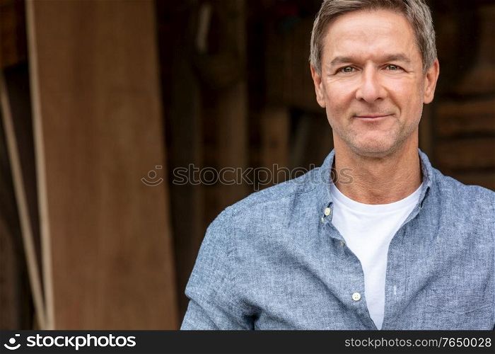 Portrait shot of an attractive, successful and happy middle aged man male wearing a blue shirt leaning on a post by a garage or barn