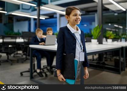 Portrait smart little smiling businesswoman looking at camera with children coworker on background. Portrait of smart little smiling business girl