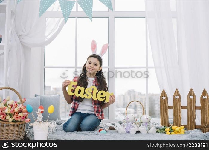 portrait smiling girl sitting front window showing yellow easter word