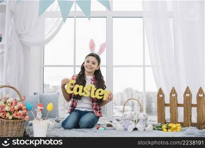 portrait smiling girl sitting front window showing yellow easter word