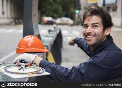 portrait smiling male electrician pointing with hard hat equipment street