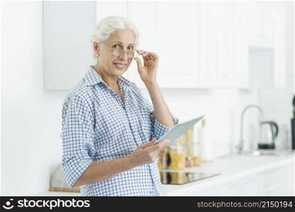 portrait smiling senior woman holding digital tablet standing kitchen