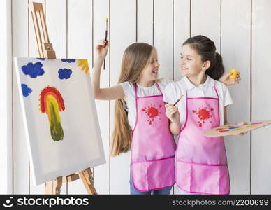 portrait smiling two girls pink apron making fun while painting canvas