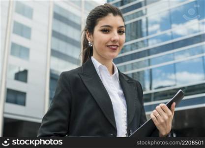 portrait smiling young businesswoman standing front building