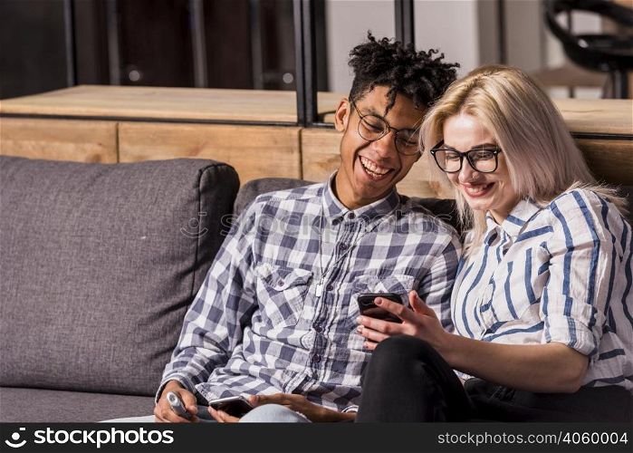 portrait smiling young couple sitting sofa looking mobile phone
