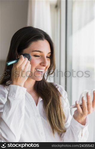 portrait smiling young woman applying face powder with makeup brush