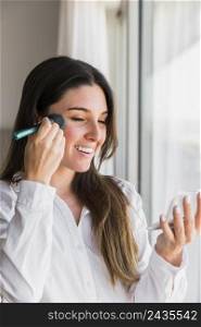 portrait smiling young woman applying face powder with makeup brush