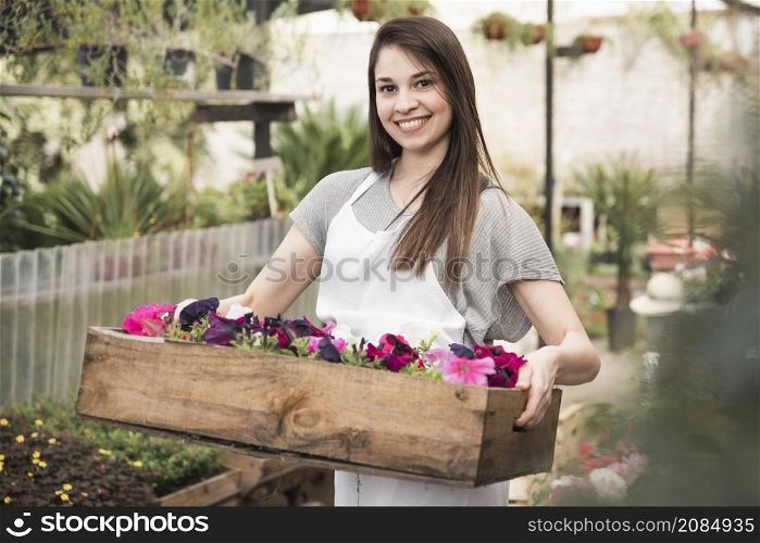 portrait smiling young woman holding colorful petunias wooden crate