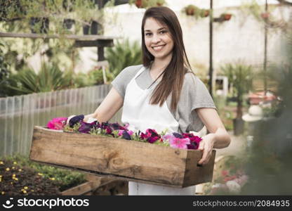 portrait smiling young woman holding colorful petunias wooden crate